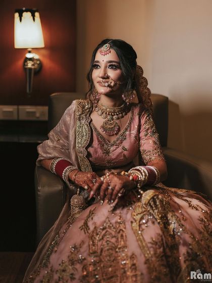 An elegant portrait of the bride seated in her pastel pink lehenga, looking poised and beautiful.