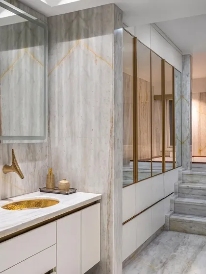 The master bathroom is clad in white Michelangelo marble, with a custom vanity featuring brass fixtures and a hammered brass sink. Mirrored cabinets enhance the room's brightness and sense of luxury.