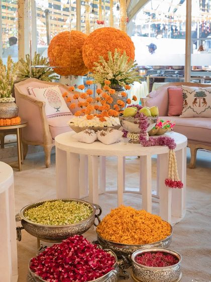 Bowls of fresh flower petals and marigold arrangements on a coffee table, ready for guests to shower the couple with blessings.