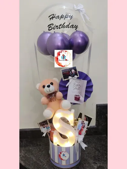 Make a statement with our personalized balloon hampers. This one features a custom "Happy Birthday" balloon, a soft teddy bear, and a light-up initial, all arranged in a charming striped box.