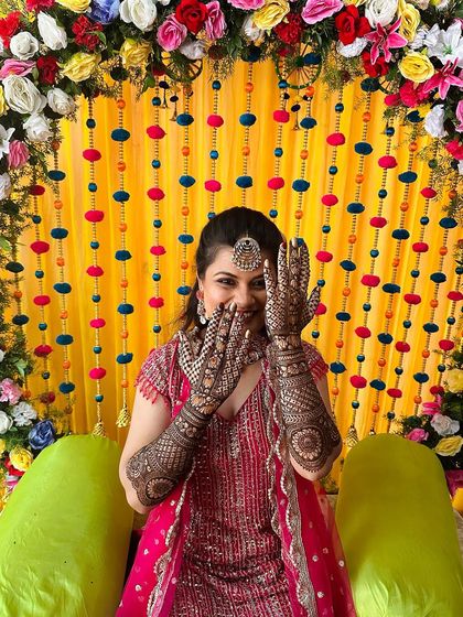 A vibrant and happy bride against a colorful backdrop, her hands framing her smiling face to show off her beautiful mehndi.