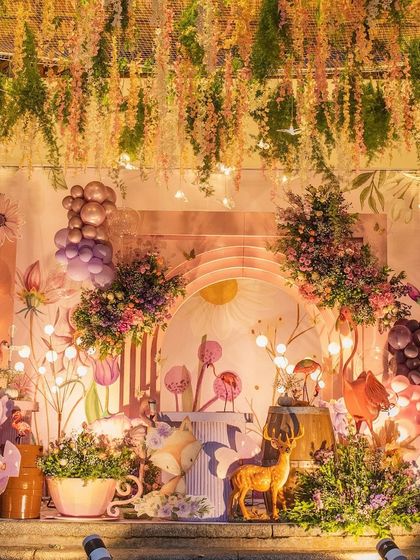 Hitanshi's enchanted garden party, featuring a stunning backdrop of illustrated flowers and a ceiling of hanging wisteria. The scene is filled with deer props, glowing lights, and magical details.