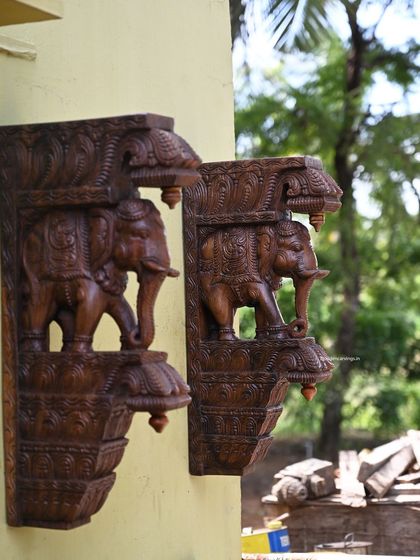 A pair of 24-inch standing elephant brackets with a fine wax brown finish, shown mounted on an exterior wall. Their sturdy design and classic finish make them suitable for both indoor and outdoor use.