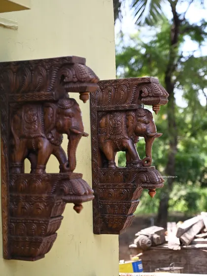 A pair of 24-inch standing elephant brackets with a fine wax brown finish, shown mounted on an exterior wall. Their sturdy design and classic finish make them suitable for both indoor and outdoor use.