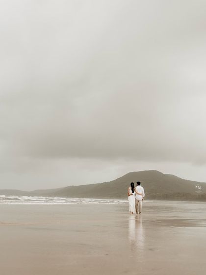 Walking towards the ocean together. This wide shot captures the couple against a dramatic, cloudy sky and rolling hills, symbolizing the start of their grand journey.