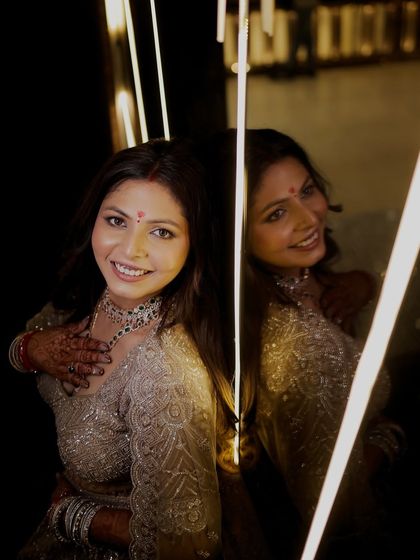 The bride smiles, her reflection captured beside her against a backdrop of warm lights. This shot highlights her happiness and the festive ambiance.