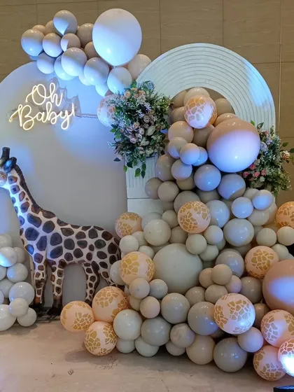 A wild and chic "Oh Baby" shower with a safari twist. A large giraffe prop stands next to a cascade of neutral-toned balloons with giraffe print accents.