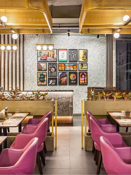 A view of the booth seating at Pasta Street, separated by low planters that add a touch of green. In the background, a gallery wall of framed prints and our custom-made rectangular lights create layers of visual interest.