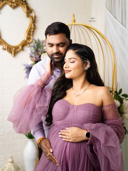 A serene portrait of the mother-to-be, with her partner's gentle touch. The off-the-shoulder purple gown and delicate hairpiece add a touch of ethereal beauty.