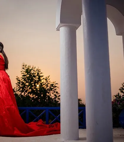 A classic romantic portrait of Yash and Priyanshi at sunset. Her flowing red gown stands out beautifully against the white pillars and the warm colors of the evening sky.