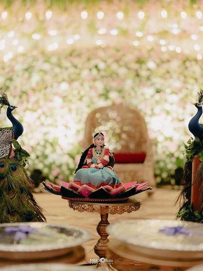 A stunning shot of a doll centerpiece surrounded by peacocks, with a massive floral backdrop creating a beautiful bokeh effect.