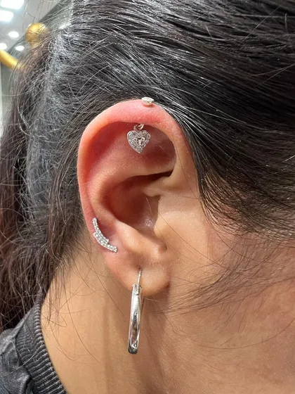 A simple yet romantic ear stack with a heart-shaped hanging on the helix and a curved bar stud on the conch.
