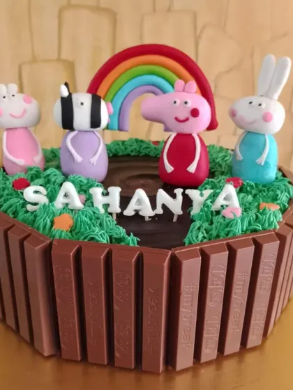 Here's a fun Peppa Pig cake, perfect for a toddler's birthday. I used KitKats to create a playful fence around a muddy puddle scene, with hand-molded fondant figures of Peppa and her friends under a bright rainbow.