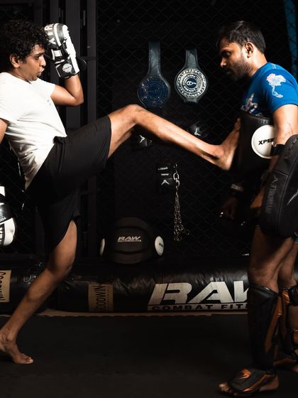 A fighter practices a teep kick on the pads held by a coach, demonstrating control and balance.