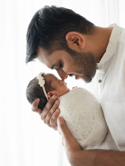 A father holds his swaddled newborn daughter, their noses touching in a sweet gesture. This is a classic and heartwarming father and newborn pose.