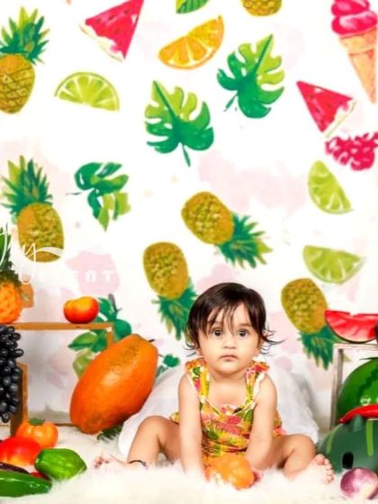 A bright and colorful tropical theme for a baby girl's photoshoot. The backdrop is filled with pineapples and citrus prints, and the set is decorated with real fruits for a fun, summery vibe.