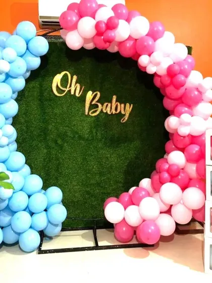 A baby shower decoration with a faux grass backdrop. The pink and blue balloon arch and 'Oh Baby' sign create a fresh, garden-party feel.