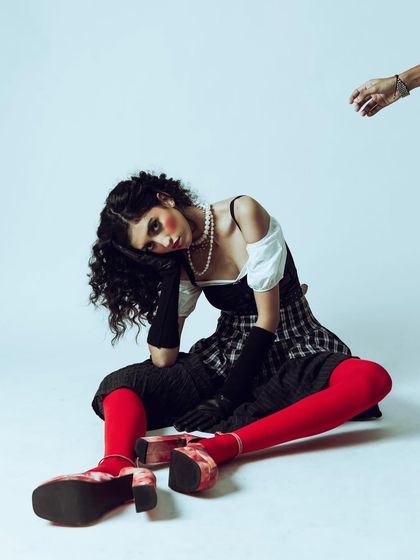 A wider view of the "vintage doll" setup, showing the full outfit from the platform shoes to the layered skirt. The pose is intentionally awkward and disjointed, fitting the theme of the shoot.