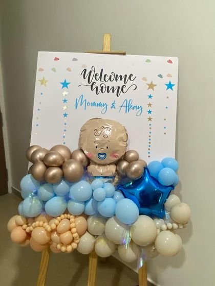 A personalized welcome easel for "Mommy & Akay." This cute sign is adorned with a garland of blue, white, and sand-colored balloons and features a baby-shaped foil balloon, making it a perfect photo prop.