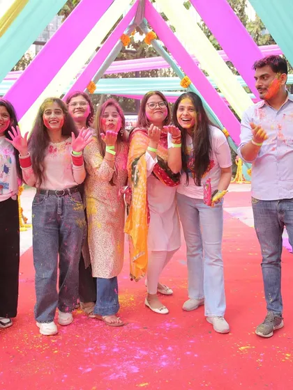 Employees enjoying the festivities under a colorful draped canopy at the IndiaMart corporate Holi celebration. This image shows a candid moment of fun and interaction.