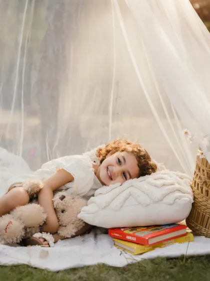 A little girl relaxes with her teddy bear and a stack of books. This lifestyle shot captures the quiet, sweet moments of childhood.