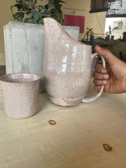 A beautiful speckled white pitcher and matching cup, perfect for serving water or juice. The glaze gives it a rustic, earthy feel.