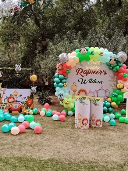 An outdoor "Wild One" first birthday party. This jungle-themed setup includes a large backdrop, animal cutouts, and balloon arrangements scattered on the lawn.