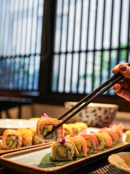 The perfect pick. A hand lifts a piece of our Rainbow Roll, highlighting the fresh ingredients and beautiful construction that makes it a favorite for both its taste and appearance.