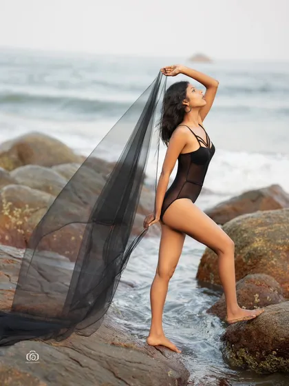 A powerful pose on the rocks, with the model holding the sheer black fabric like wings. This shot is both graceful and strong, perfect for a high-fashion concept.