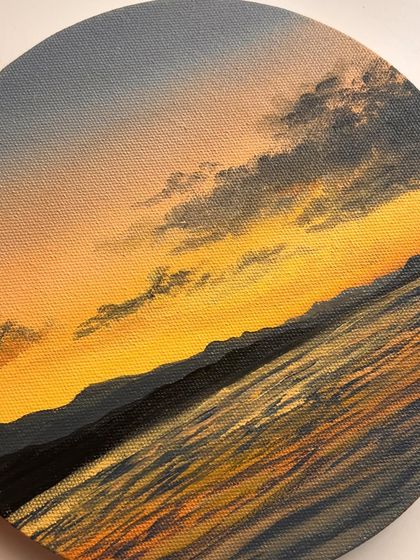 A close up of my yellow sunset painting on a round canvas. The texture of the water and the soft blending of the yellow and grey sky create a peaceful scene.