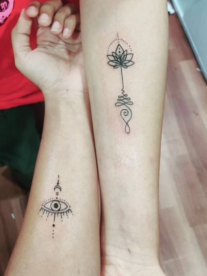 Matching minimalist tattoos, one of an evil eye and the other a lotus unalome.