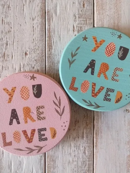 A duplicate of 85, "You are loved." These magnets feature a folksy, patterned font and botanical details, available in soft pink and blue.