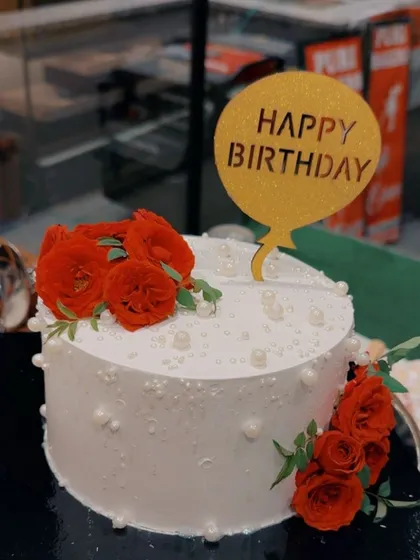 A closer look at one of my classic floral cakes. This 100% eggless white cake is decorated with delicate pearl-like details and fresh red roses, topped with a golden "Happy Birthday" balloon sign. It's a simple yet elegant design that is perfect for anniversaries and birthdays.