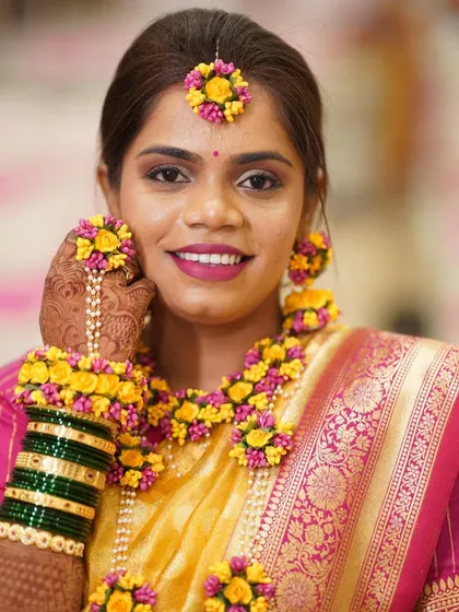 A beautiful Haldi bride adorned with fresh floral jewelry. The makeup is kept soft and natural with a pop of pink on the lips to complement the yellow flowers.
