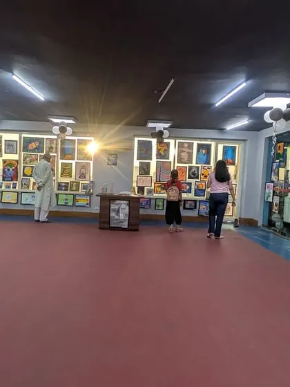 A panoramic view of the exhibition hall, bustling with students, parents, and art lovers. The spacious layout allows everyone to comfortably enjoy the diverse range of paintings and drawings on display.