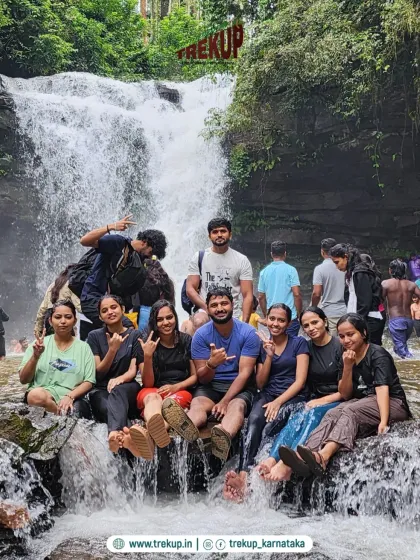 A group of friends sitting on rocks in front of a waterfall, cooling off and having a great time.