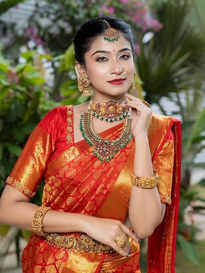 A radiant bride in a classic red saree, perfectly complemented by our temple jewellery set with green and red kemp stones. This is a timeless look for any South Indian wedding.