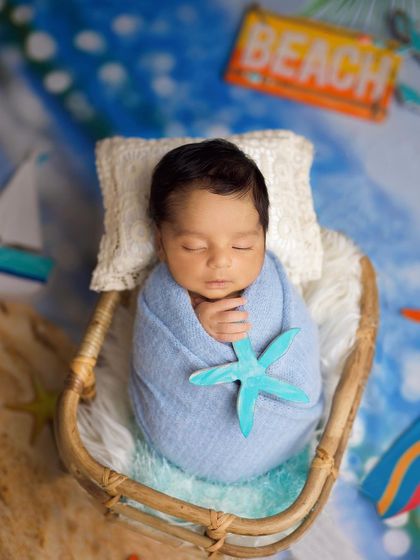 A close-up of the beach-themed newborn setup, focusing on the baby swaddled in blue and holding a starfish prop.