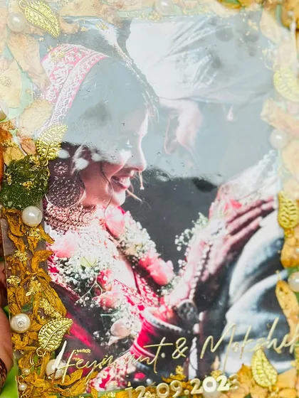 A beautiful varmala preservation in a 5x7 inch rectangular plate. The couple's photo is framed by their wedding flowers, golden leaves, and pearls, with their names engraved below.