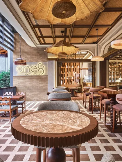 A view from the terrace, looking back into the restaurant. The brand's glowing logo is set against a brick wall, and custom-designed tables with gear-like edges add a playful, industrial touch.