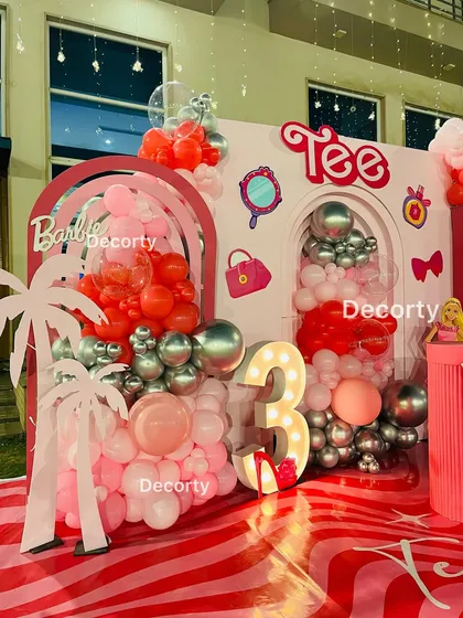 A close-up of the left side of the Barbie backdrop, showing the layered arches, balloon cascades, and the illuminated number '3'.