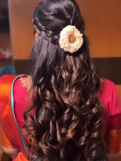 A beautiful half-up style with a braided detail and a single flower, with the rest of the hair in defined curls.