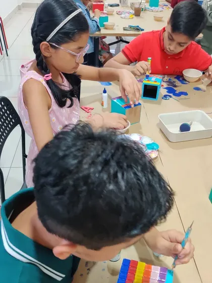 A close-up view of the creative action, showing kids gluing tiles and painting their personalized pen stands.