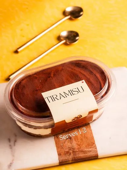 A stylish shot of our Tiramisu tub, ready to be enjoyed with two golden spoons. It's the perfect shareable personal dessert.