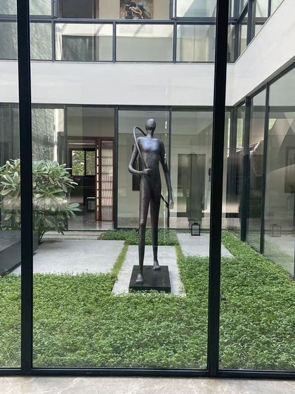 A frontal view of the modern sculpture in a minimalist farmhouse courtyard. The clean lines of the architecture and landscape frame the artwork, making it the undeniable hero of the space.