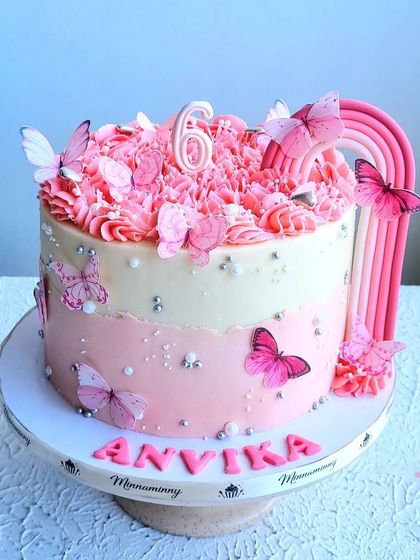 A beautiful butterfly and rainbow cake in shades of pink. The cake features an ombre design, a pink rainbow, and is adorned with delicate, edible butterflies.