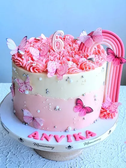 A beautiful butterfly and rainbow cake in shades of pink. The cake features an ombre design, a pink rainbow, and is adorned with delicate, edible butterflies.