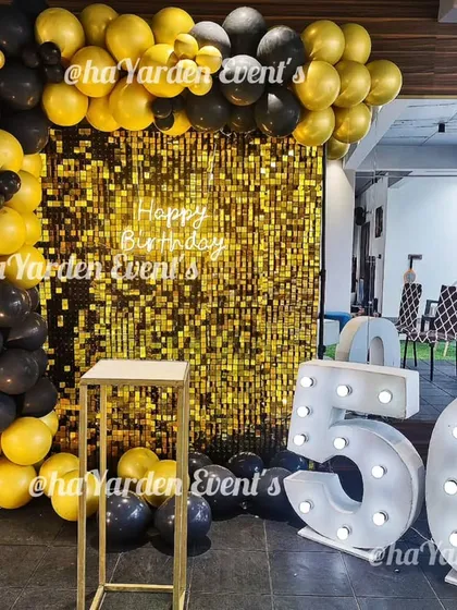 Celebrating 50 in style. This party decor in a modern space features a gold sequin backdrop, large marquee numbers, and a black and yellow balloon arch.