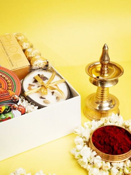 A close-up of the 'Jamanthi Poo' hamper next to a traditional brass nilavilakku. This image connects the modern gift with the timeless traditions of the Onam festival.