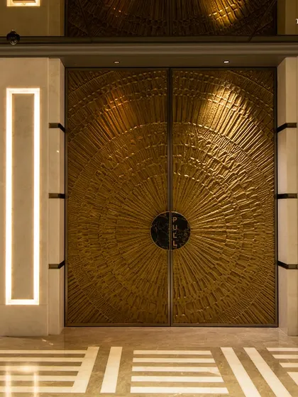 The ornate, custom-designed brass doors of the theater at Maison INOX. These doors are a work of art in themselves, reflecting the contemporary take on Art Deco that defines the entire space.